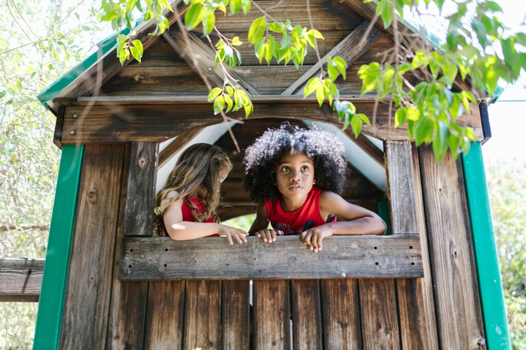 Two children playing in a wooden cabin surrounded by nature